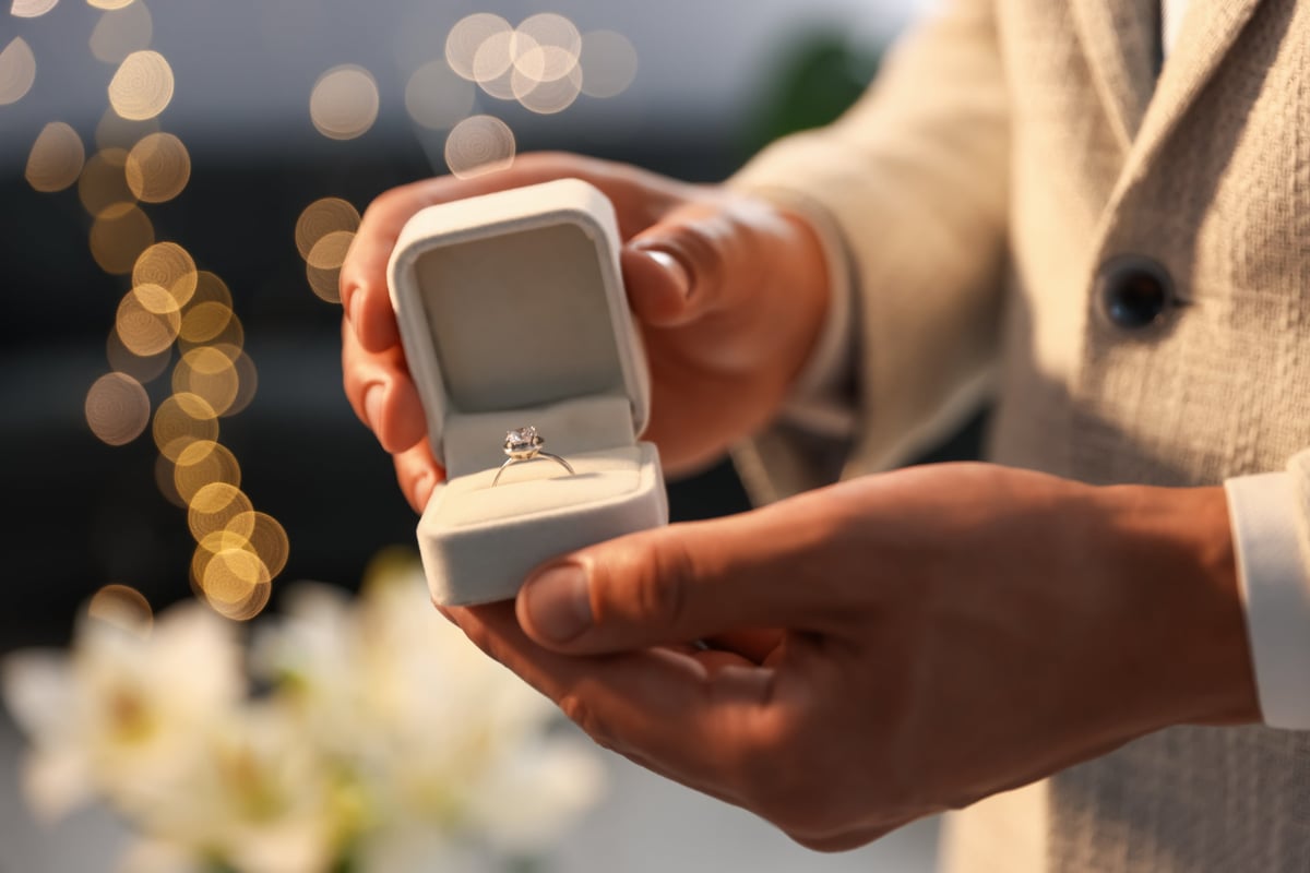 Hands holding an engagement ring against a warm, softly blurred background