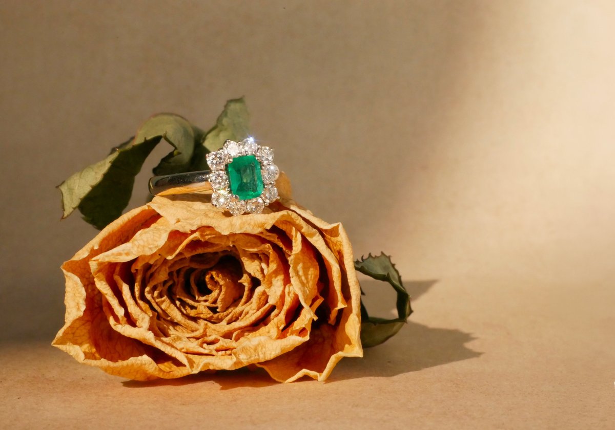 Emerald and diamond engagement ring on a dried rose